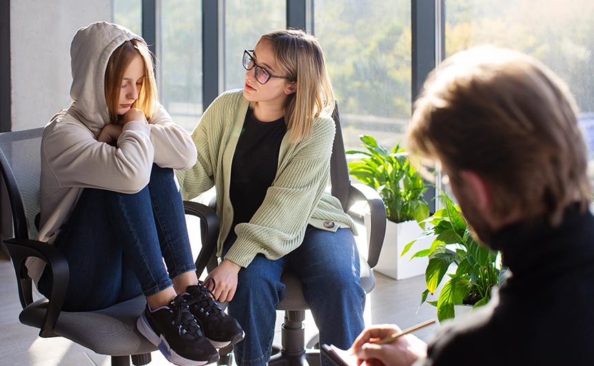 Teen in Hoodie Comforted by Counselor in Sunlit Office