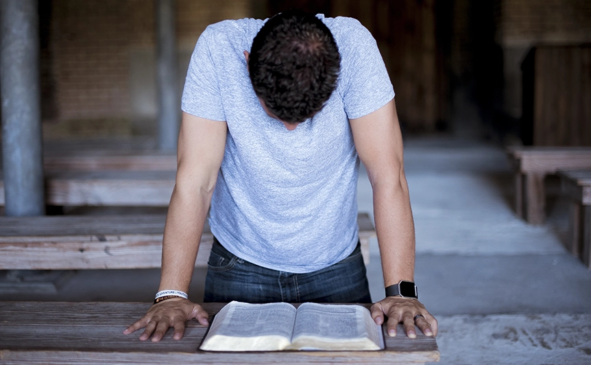 Man Praying Over Open Bible in Church Setting