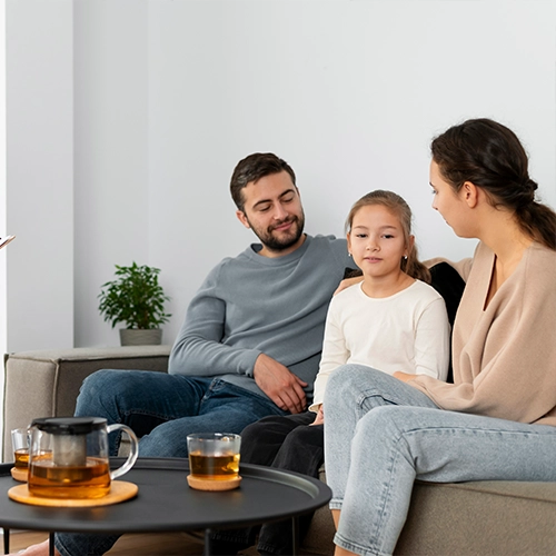 Family sitting together on a couch with tea on a table.