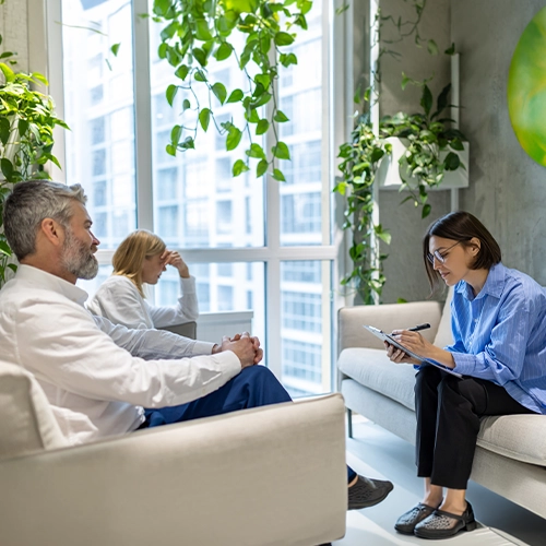 Group counseling session in a modern office with large windows and plants.