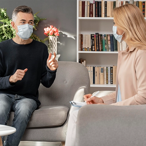 Man and woman wearing masks talking in a counseling session.