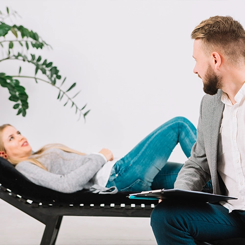 Woman on therapy couch talking to counselor with clipboard.
